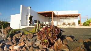 Een modern huis met een witte gevel, een houten pergola en een tuin met cactussen en vetplanten.