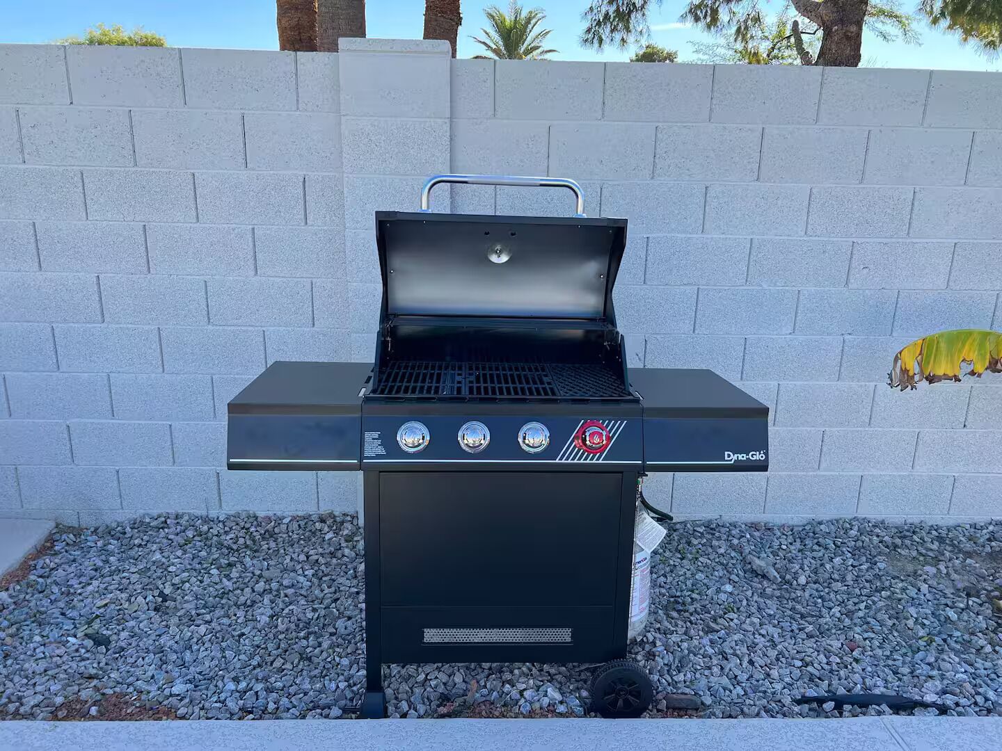 Ein schwarzer Grill für den Außenbereich mit vier Reglern und einem digitalen Display, vor einer Steinwand mit einem kleinen Garten.