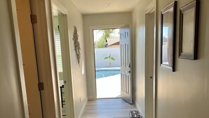 A hallway with wooden flooring, a door leading to a pool, and framed pictures on the wall. - Modern Oasis in the Desert (Tempe)