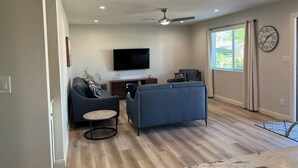A modern living room with a flat-screen TV, a ceiling fan, and a large window with curtains. - Modern Oasis in the Desert (Tempe)