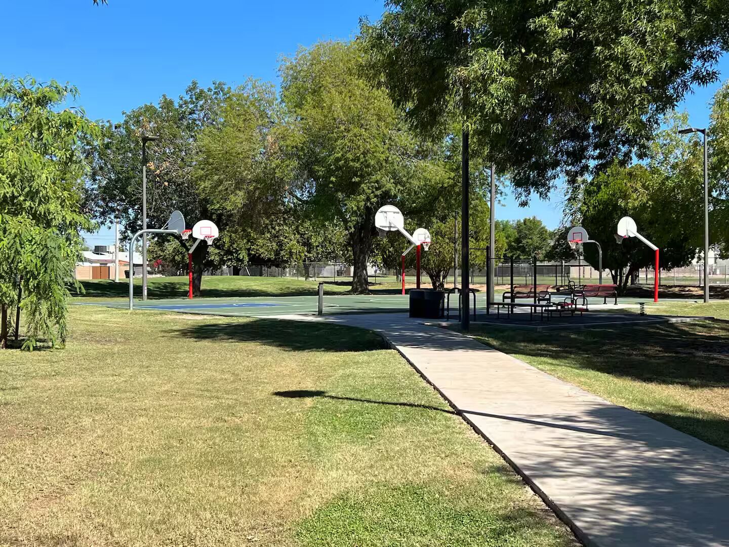 Una cancha de baloncesto con tres aros, rodeada de árboles y un cielo despejado.