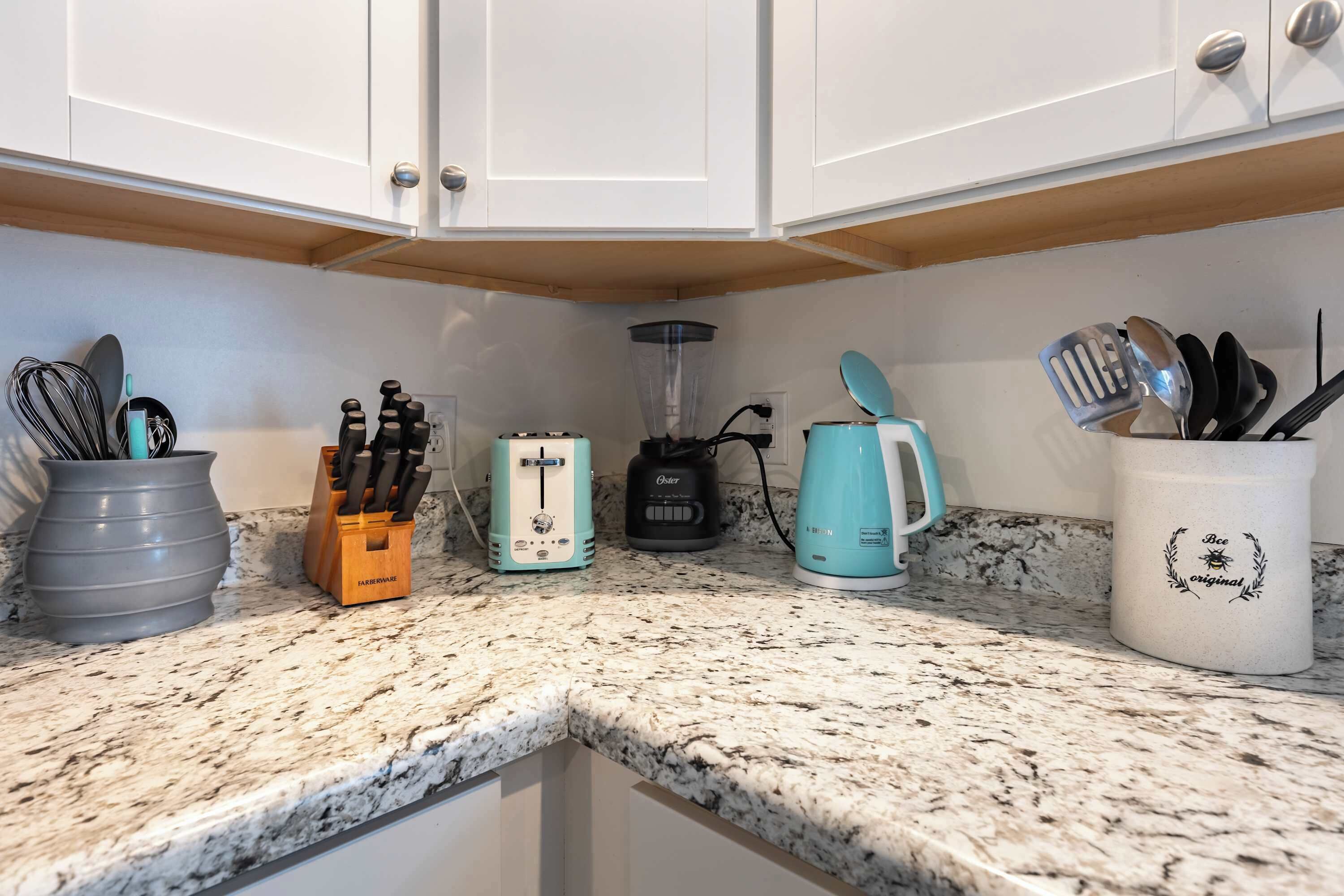 A kitchen with white cabinets, a granite countertop, a coffee maker, a blender, a toaster, and a utensil holder.