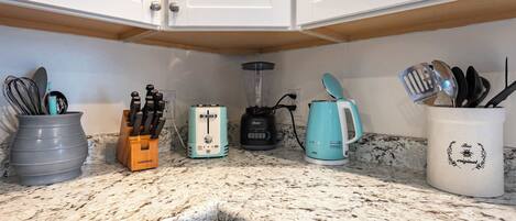 A kitchen with white cabinets, a granite countertop, a coffee maker, a blender, a toaster, and a utensil holder.