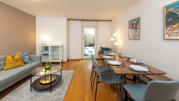 Een moderne woonkamer met een bank, salontafel en een eethoek met stoelen en een tafel gedekt voor twee personen.
