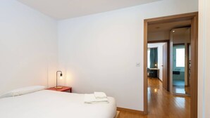 Een hotelkamer met een bed, een nachtkastje, een lamp en uitzicht op de gang en een andere kamer.