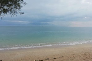 Uma praia com areal arenoso e mar calmo sob um céu nublado.