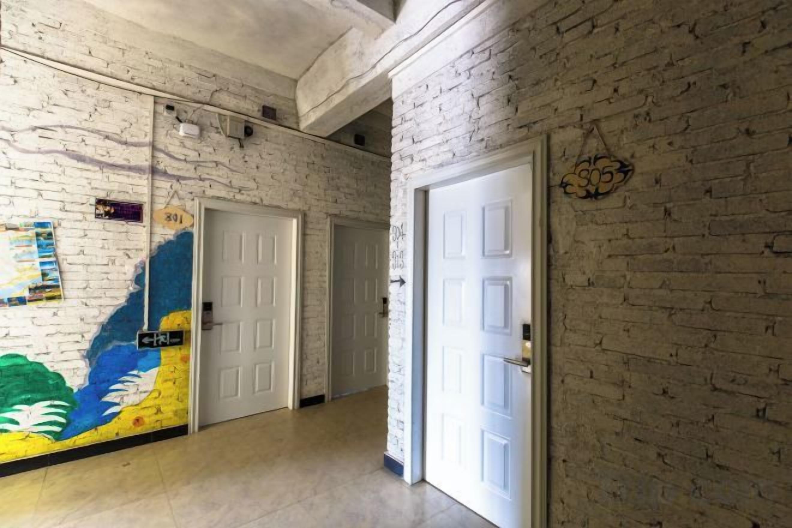 A hallway with white brick walls, white doors, and a mural on the left wall.