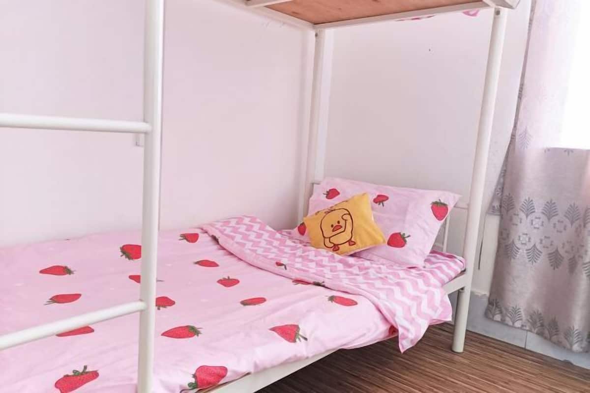 A bunk bed with a pink bedspread featuring strawberry patterns, a yellow pillow with a cartoon character, and a white metal frame.