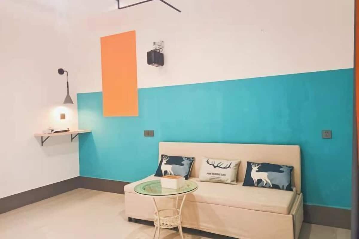 A room with a sofa, a small round table, a wall-mounted shelf, and a wall light.
