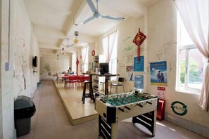 Une pièce avec une table de baby-foot, des ventilateurs de plafond, un téléviseur et une fenêtre avec des rideaux.