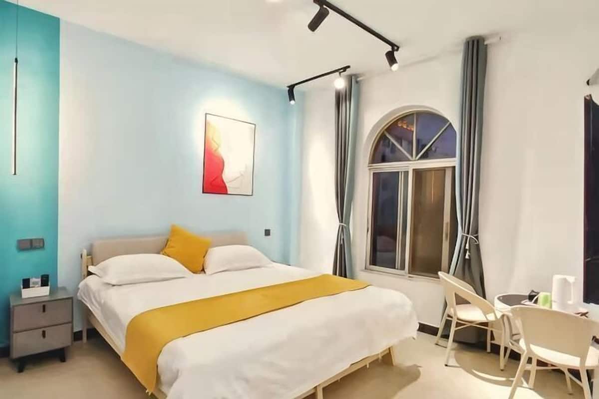 A bedroom with a bed, bedside table, and a window with curtains.