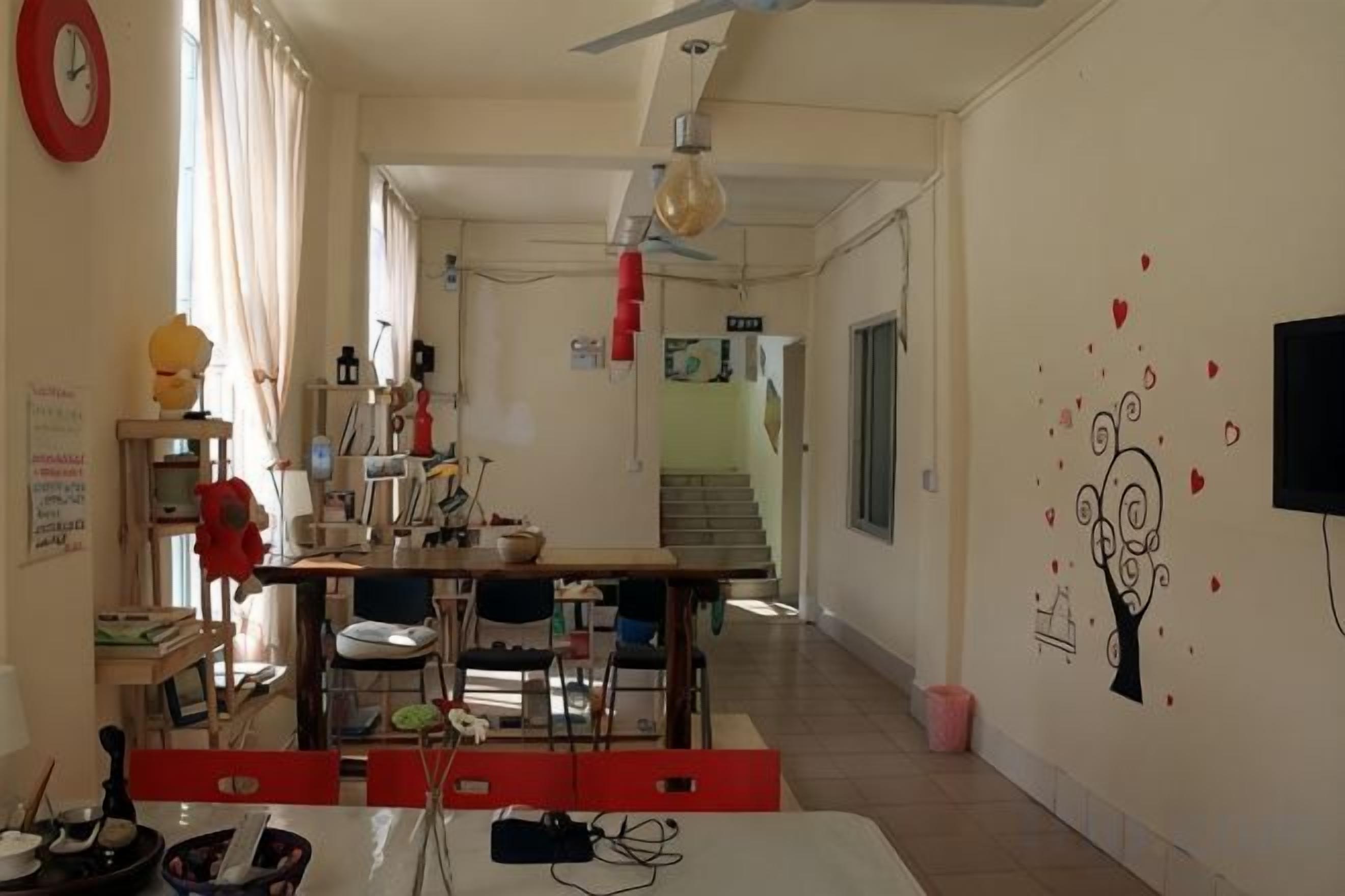 A room with a dining table, chairs, a red sofa, a TV, and a wall with a tree and hearts mural.