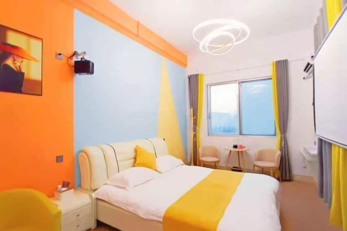 A hotel room with a bed, bedside table, chair, and a window with curtains.