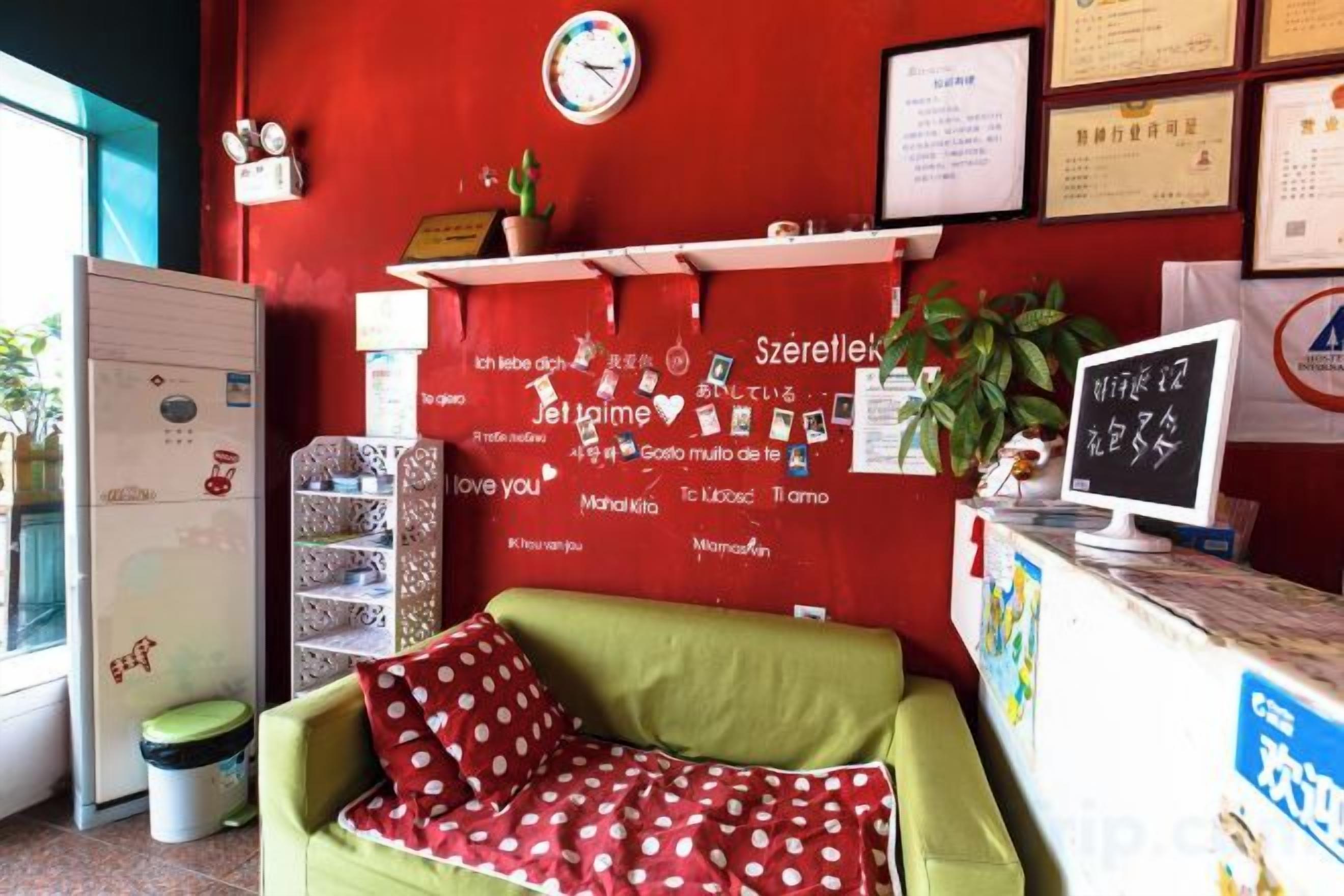 A reception area with a red wall, a green sofa, a white desk, and a clock.
