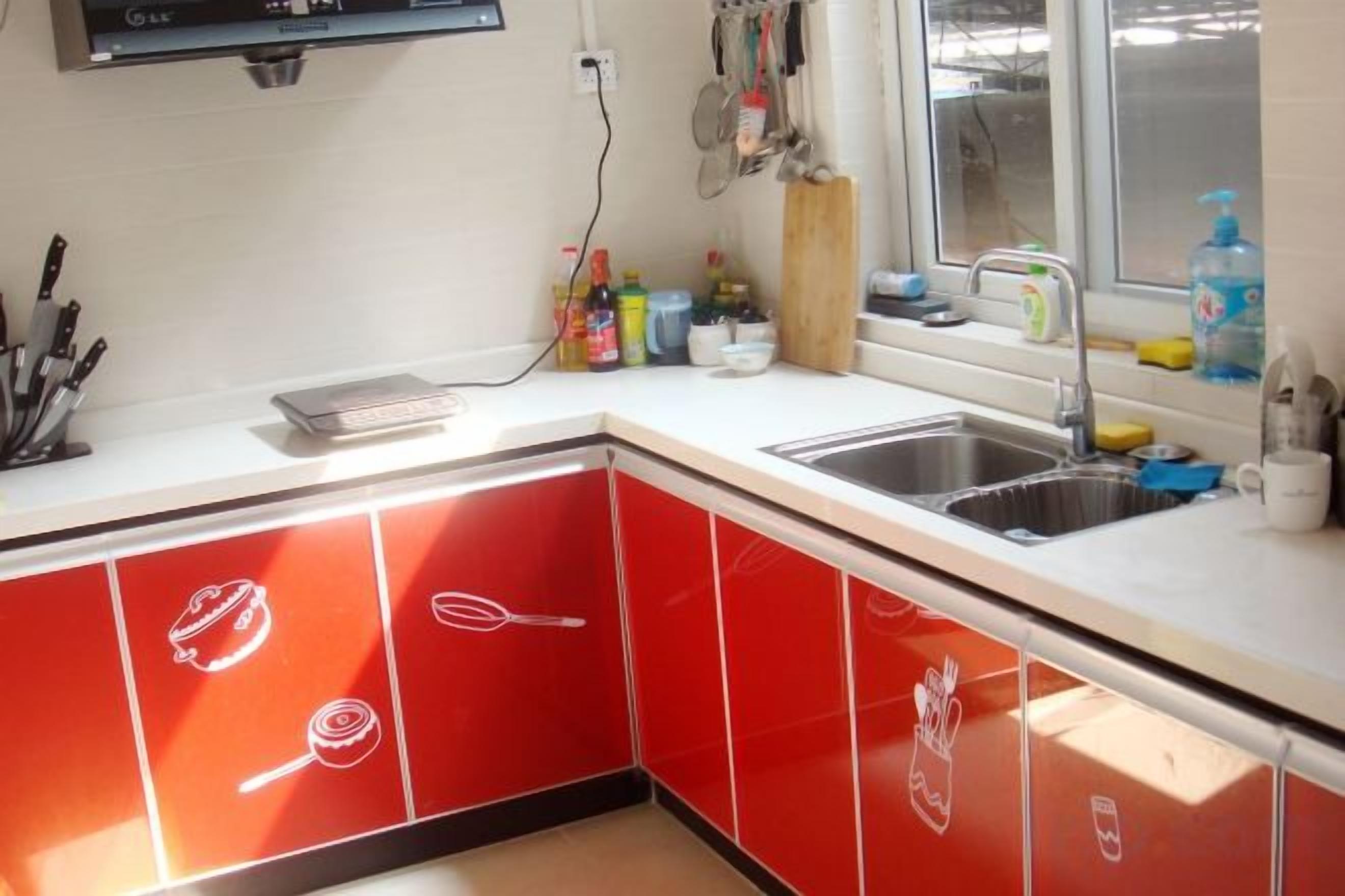A kitchen with red cabinets, a sink, and various kitchen utensils.
