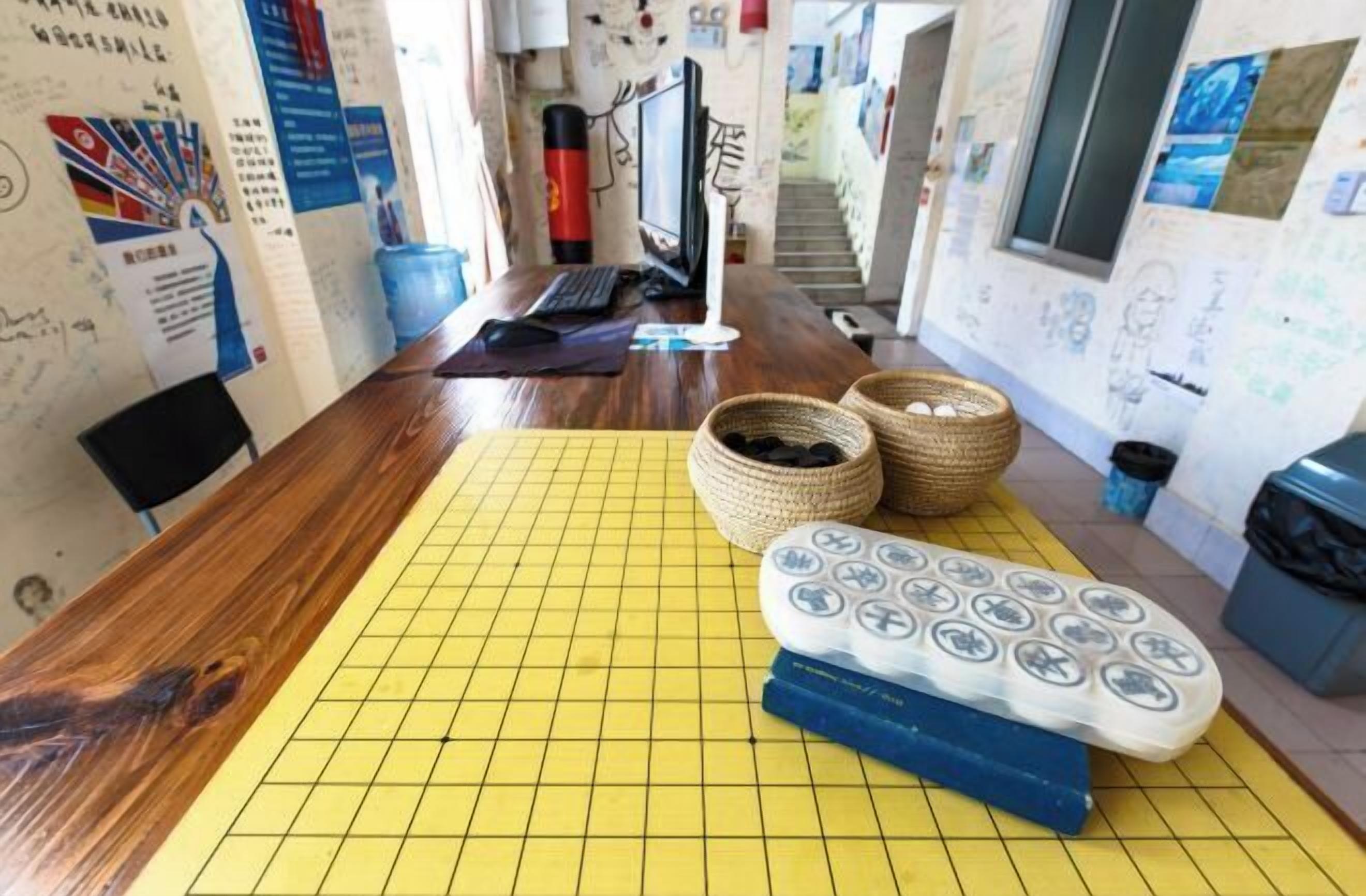 Un espace de travail comprenant un bureau en bois, un tapis à motifs quadrillés jaunes, un clavier, un écran et des paniers.