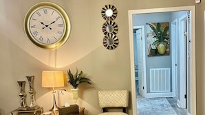 Una sala de estar con sofá, reposapiés, mesa, lámpara y un reloj de pared.