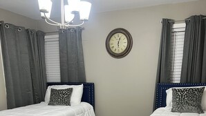 Una habitación de hotel con dos camas, un candelabro, un reloj y una ventana con cortinas.