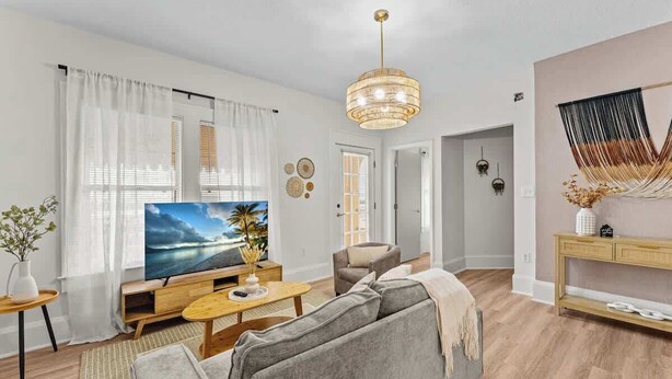 En moderne stue med et stort fladskærms-tv, en grå sofa, et træbord og en hængende lampe.