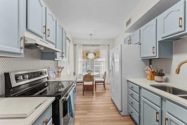 A modern kitchen with light blue cabinets, a stainless steel refrigerator, and a wooden dining table with chairs. - 304 Lakeshore - Unit 1 and 2 (Kissimmee)
