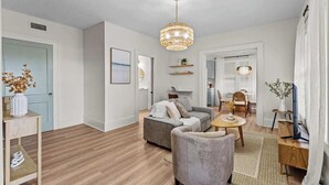 En moderne stue med en grå sofa, et lille rundt bord og en lysekrone.