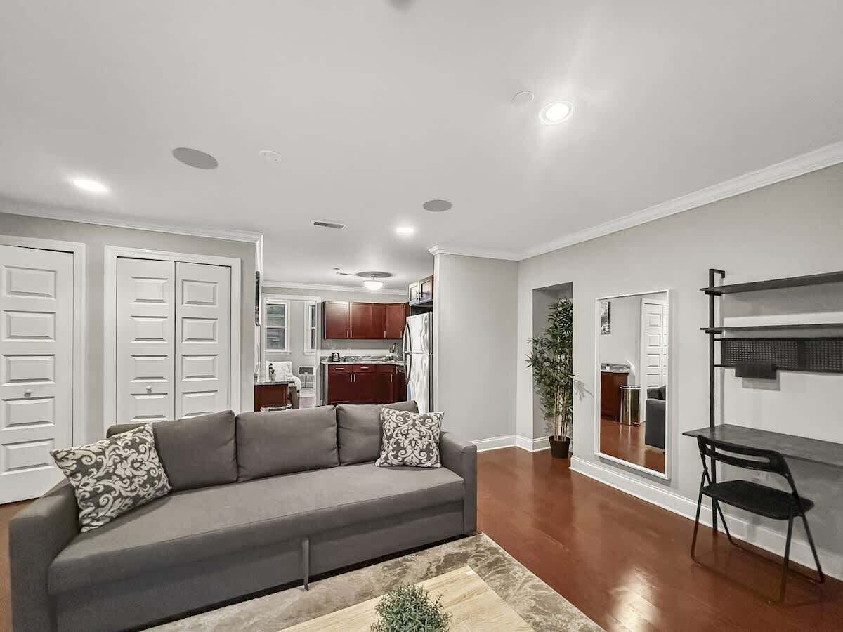 A modern living room with a grey sofa, white doors, and a kitchen in the background.