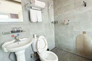 A bathroom with a pedestal sink, toilet, and shower. There is a towel rack above the sink and a toilet paper holder below it.