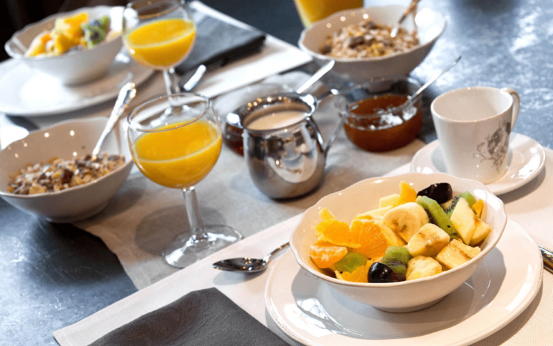 A breakfast setting with bowls of cereal, a glass of orange juice, and a bowl of fruit salad.
