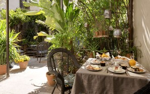 An outdoor dining area with a table set for a meal, surrounded by potted plants and a wicker chair. - Exclusive B&B Suites, Apartments, Spa & Fitness<br>The Augustinian House an (AVIGNON)