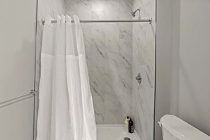 Une salle de bain moderne avec une douche à parois de verre, des carreaux de marbre, des toilettes et un porte-serviettes.