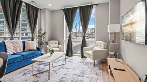 Una sala de estar moderna con un sofá azul, sillones blancos, una mesa de centro y un banco de madera.