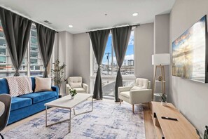 Un salon moderne avec un canapé bleu, des fauteuils blancs, une table basse et un banc en bois.