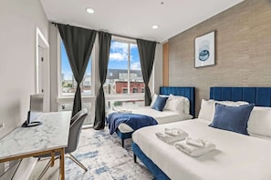Een hotelkamer met twee bedden, een bureau en een groot raam met gordijnen.