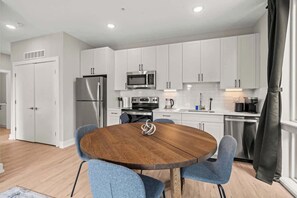 Een moderne keuken met witte kasten, roestvrijstalen apparatuur en een ronde houten tafel met blauwe stoelen.