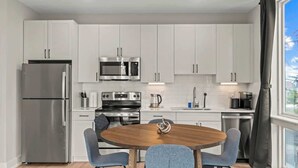 Una cocina moderna con armarios blancos, electrodomésticos de acero inoxidable y una mesa de madera redonda con cuatro sillas.
