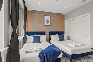 Une chambre d’hôtel avec deux lits, une grande fenêtre avec des rideaux, un tableau encadré au mur et une porte.
