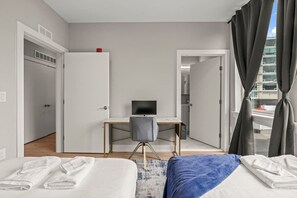 Une chambre d’hôtel moderne avec deux lits, un bureau avec une télévision et une vue sur la ville grâce à de grandes fenêtres.