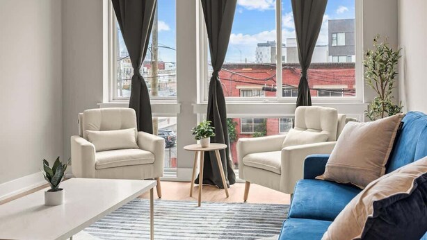 A modern living room with two beige armchairs, a blue sofa, and a small round table with a plant.