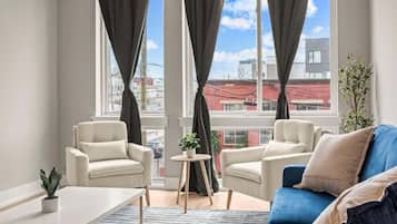 A modern living room with two beige armchairs, a blue sofa, and a small round table with a plant.