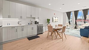 A modern kitchen with white cabinets, a dining area with a wooden table and chairs, and a living area with a blue sofa.