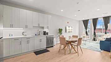 A modern kitchen with white cabinets, a dining area with a wooden table and chairs, and a living area with a blue sofa.