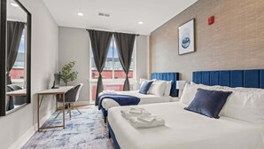 A hotel room with two beds, a desk, and a view of the city.