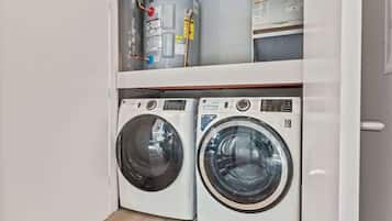 A compact laundry room with two front-loading washing machines and a water heater on the shelf above.