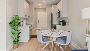 A modern kitchen with white cabinets, a dining area with a marble table, and a potted plant. - Luxury 1BD | 2 Beds | Northern Liberties (Philadelphia)