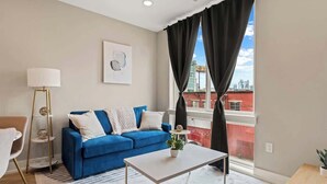 A modern living room with a blue sofa, a white coffee table, and a floor lamp. - Luxury 1BD | 2 Beds | Northern Liberties (Philadelphia)