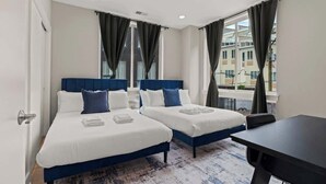 A hotel room with two beds, a desk, and a large window with curtains.