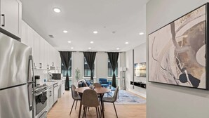 A modern kitchen with stainless steel appliances, a dining area with a round table and chairs, and a large abstract painting on the wall.