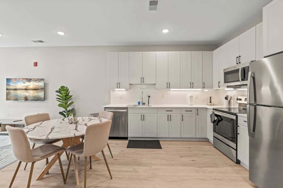 A modern kitchen with white cabinets, stainless steel appliances, and a marble dining table.