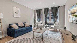 A modern living room with a blue sofa, white armchairs, a coffee table, and a large window with curtains. - Luxury 1BD | 3 Beds | Northern Liberties (Philadelphia)