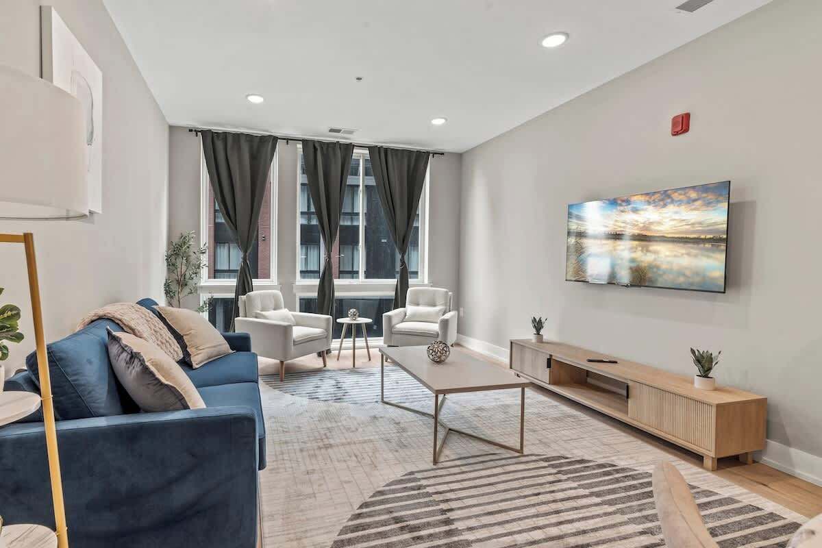 A modern living room with a blue sofa, two armchairs, a coffee table, and a TV mounted on the wall.